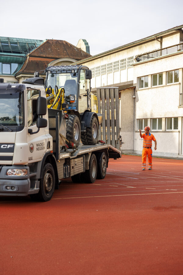 Sportplatz Waesserwies Arbeiter lotst LKW mit Bagger